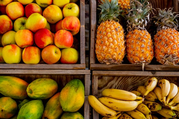 Colorful display of apples, pineapples, bananas, and papayas in wooden crates at a market.